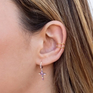 Macro view of gold ear cuff and silver hoop earring with multi-color zircon cross pendant
