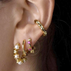 Set of gold earrings with pearls and pink gemstones shown on ear in a close-up fashion shot