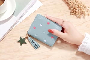 Detail of light blue faux leather wallet with heart embroidery and tassel on wood table
