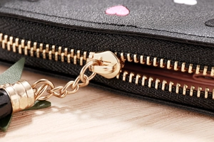 Macro detail of black leather wallet zipper with heart embroidery and gold tassel