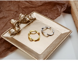 Dettaglio di anelli a onda intrecciata oro e argento su un vassoio decorativo
