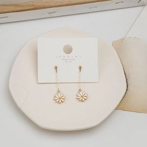 Detail of elegant daisy dangle earrings with white petals and gold chains on a ceramic tray