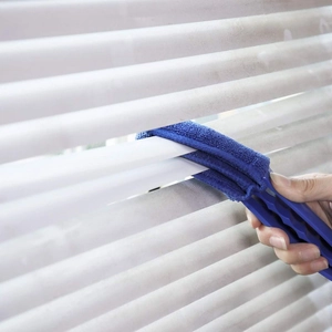 Detail view of a blue handheld microfiber cleaner wiping white window blinds