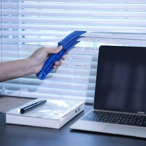 Detail showing blue microfiber window blind cleaner dusting white blinds in an office