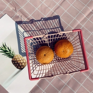 Pink metal wire storage basket with oranges on a pink checkered picnic cloth