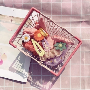 Mini metal basket filled with floral hair clips and plaid scrunchies on pink tablecloth
