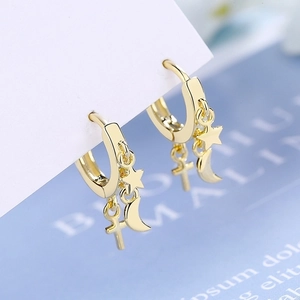 Orecchini a cerchio dorati con ciondoli a stella, luna e croce su un cartoncino bianco