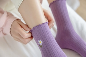 Detail of light purple ribbed mid-calf sock with daisy embroidery and wavy ruffle trim