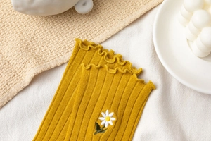 Detailed view of ginger yellow ribbed socks featuring white daisy embroidery and lace trim