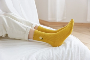 Detail of yellow ribbed crew socks with daisy embroidery and ruffled lace cuffs