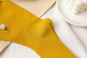 Detail of yellow ribbed knit socks featuring delicate white daisy embroidery pattern