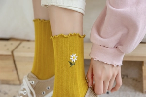 Close-up of ginger yellow ribbed socks with daisy embroidery and lettuce edge detail