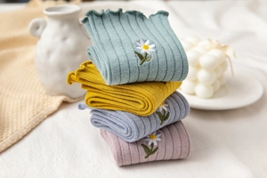 Detail of knit socks with wavy lace edges and daisy embroidery in four pastel colors