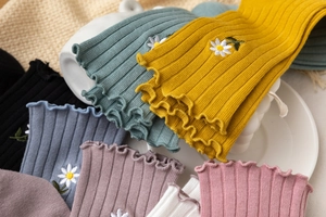 Detail of ruffled lace cuffs and daisy embroidery on soft ribbed knit crew socks
