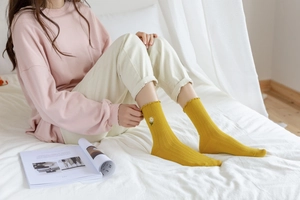 Close-up of ginger yellow mid-calf cotton socks featuring white daisy embroidery and frill trim