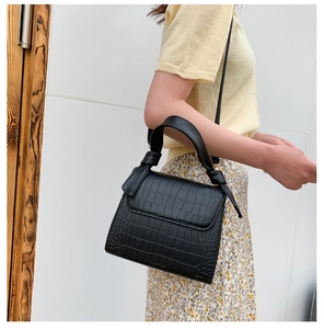 Detail of black crocodile pattern leather handbag styled with floral dress and yellow knit