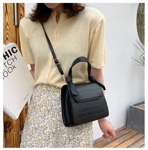 Detail of black crocodile pattern crossbody bag with a unique knot handle and flap