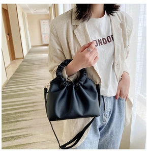 Detail of a black pleated crossbody bag featuring a soft ruched cloud-style handle and matte finish
