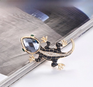 Detailed close-up of a gold lizard brooch featuring black enamel and sparkling rhinestones
