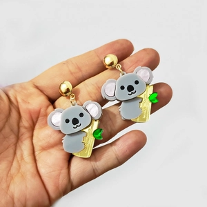Detail of adorable koala earrings with green leaves held in hand against white background