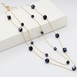 Collar largo dorado con cuentas de cubos azul profundo sobre una caja blanca