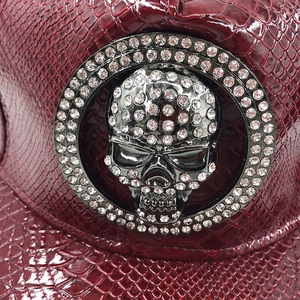 Macro shot of rhinestone skull emblem and faux crocodile texture on burgundy leather cap