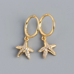 Macro detail of gold starfish earrings with sparkling zircon stones on grey background