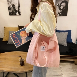 Pink canvas tote bag detail featuring white woven label text in a cozy cafe setting