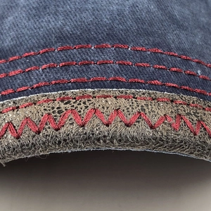 Detailed macro view of denim fabric with brown leather piping and red contrast stitching