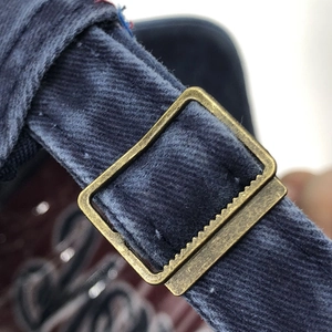 Close-up of adjustable brass metal buckle on a navy washed cotton baseball cap strap