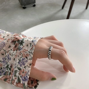 Macro shot of minimalist 925 sterling silver twisted ring on finger with floral sleeve