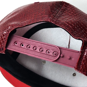 Dettaglio del cappellino in pelle rossa con trama a coccodrillo e chiusura snapback