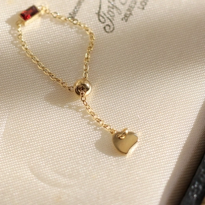 Macro shot of 18K gold chain ring with emerald-cut red stone and heart charm detail