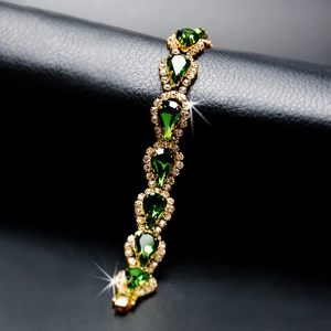 Bracelet doré luxueux avec cristaux vert émeraude en goutte sur fond cuir sombre