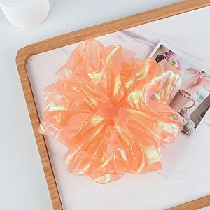 Detail of peach iridescent organza scrunchie on marble background with elegant textures