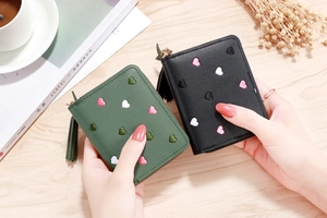 Detail of short PU leather wallets with embroidered hearts and tassel zippers in a lifestyle setting