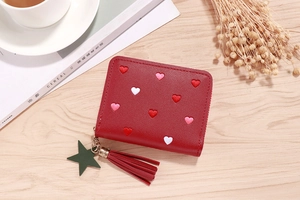 Close-up of red PU leather wallet with heart embroidery and tassel on a wooden desk