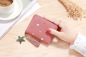 Pink PU leather wallet with heart embroidery, green star charm and tassel on wood table