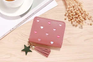 Pink PU leather wallet with heart embroidery and tassel charm on a wooden desk