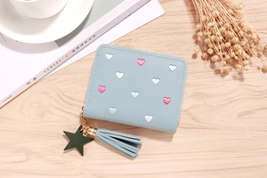 Close-up of light blue PU leather wallet with heart embroidery and tassel on wood table