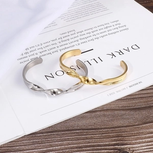 Minimalist twisted C-shape metal bangle set in gold and silver finish on a magazine