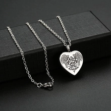 Macro shot of silver heart pendant with wings, cross, and memorial engraving text