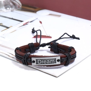 Detail view of a vintage braided leather bracelet with a metal plate engraved with Dream