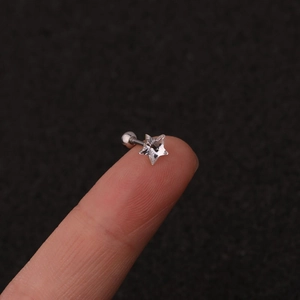 Macro shot of minimalist star-shaped crystal stud earring held on a finger for scale