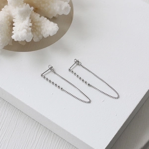 Detail view of silver tassel chain drop earrings with beads on a white textured surface