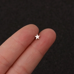 Macro shot of tiny silver star stud earring held by fingertips for size reference