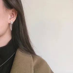 Elegant silver-tone CD letter drop earrings with delicate tassel chains on female model