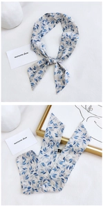 Detail of grey silk twilly scarf with blue leaf patterns on a minimalist white backdrop