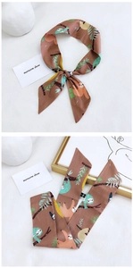 Detail of a brown skinny scarf featuring sloth and tropical leaf prints on white fabric