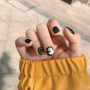 Close-up of matte black press-on nails with daisy and smiley face designs worn outdoors